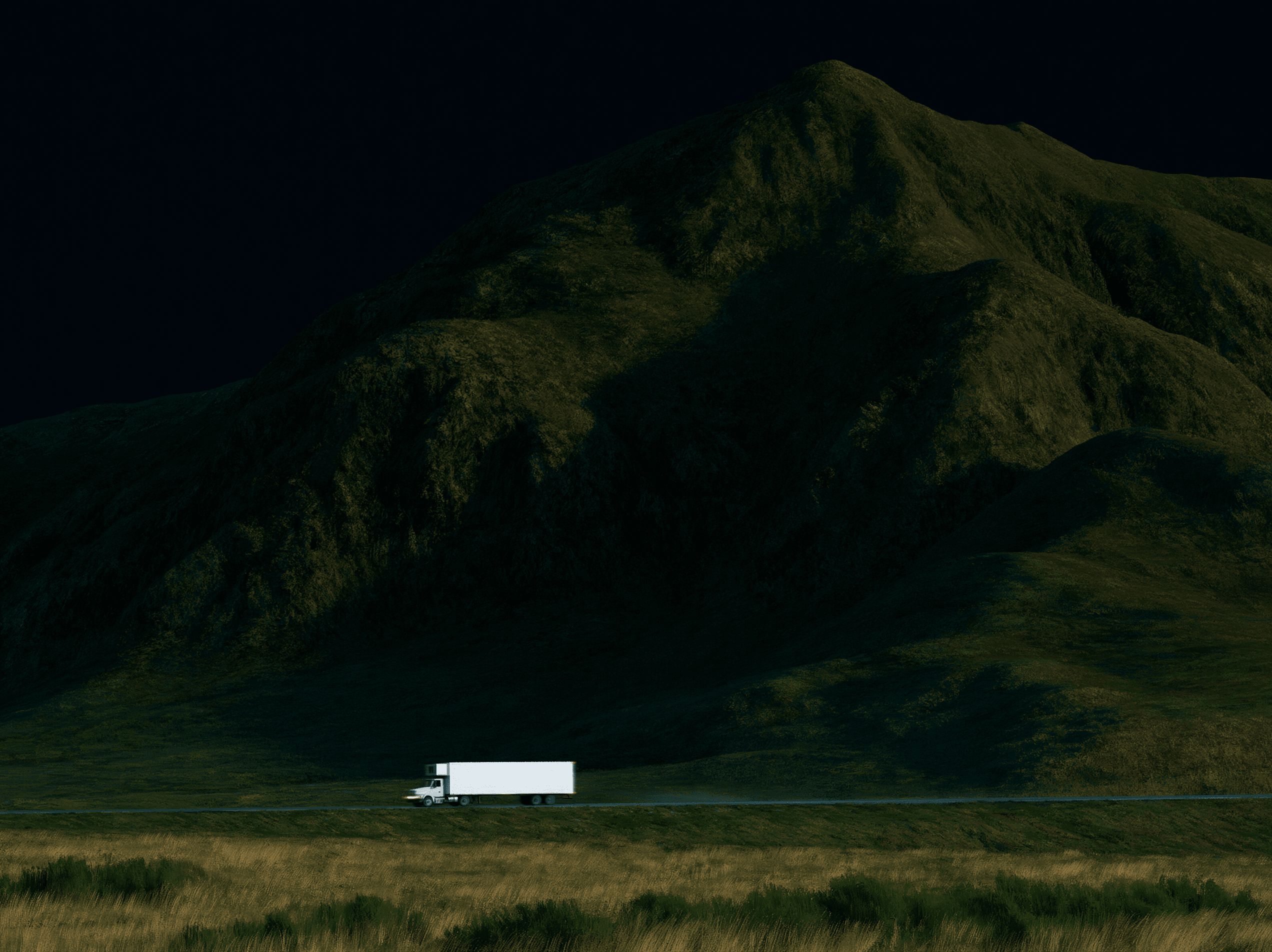 A refrigerated truck driving beneath a dark mountain landscape